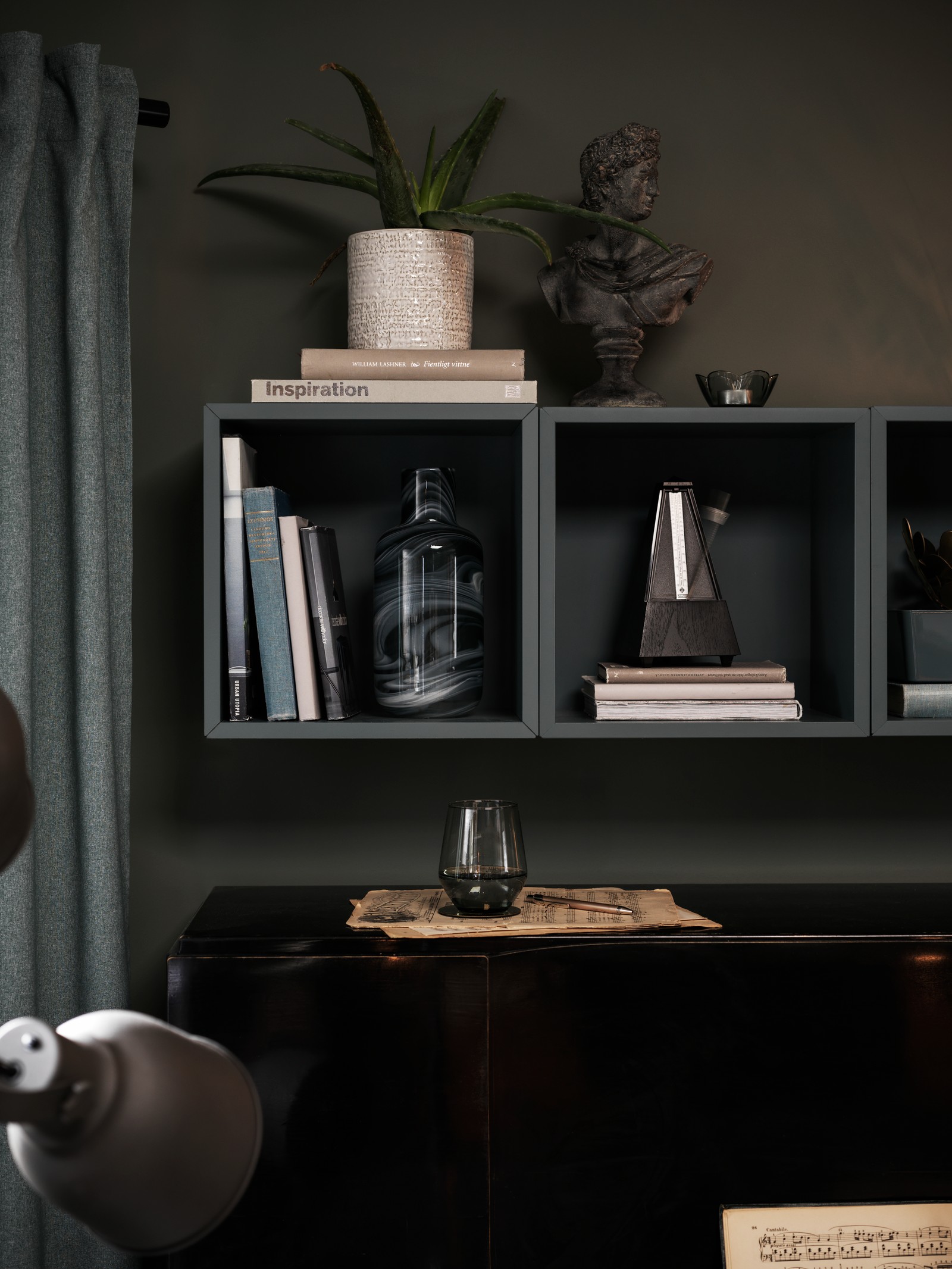A plant pot and other decorations stand on, and in, a row of grey-turquoise wall-mounted EKET cabinets above a piano.