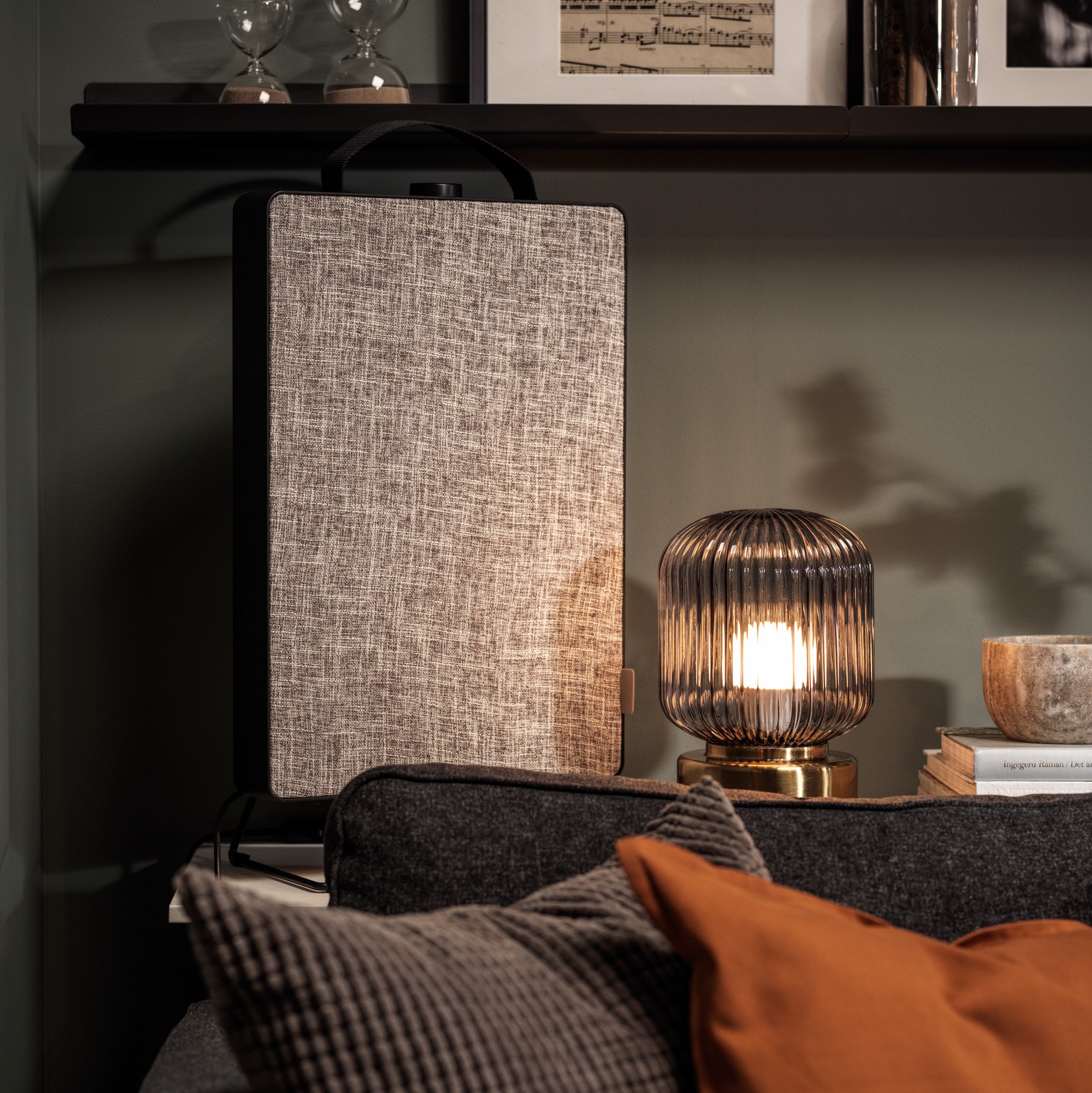 Standing on the wall shelves behind a sofa is a black FÖRNUFTIG air purifier together with framed art and decorations.