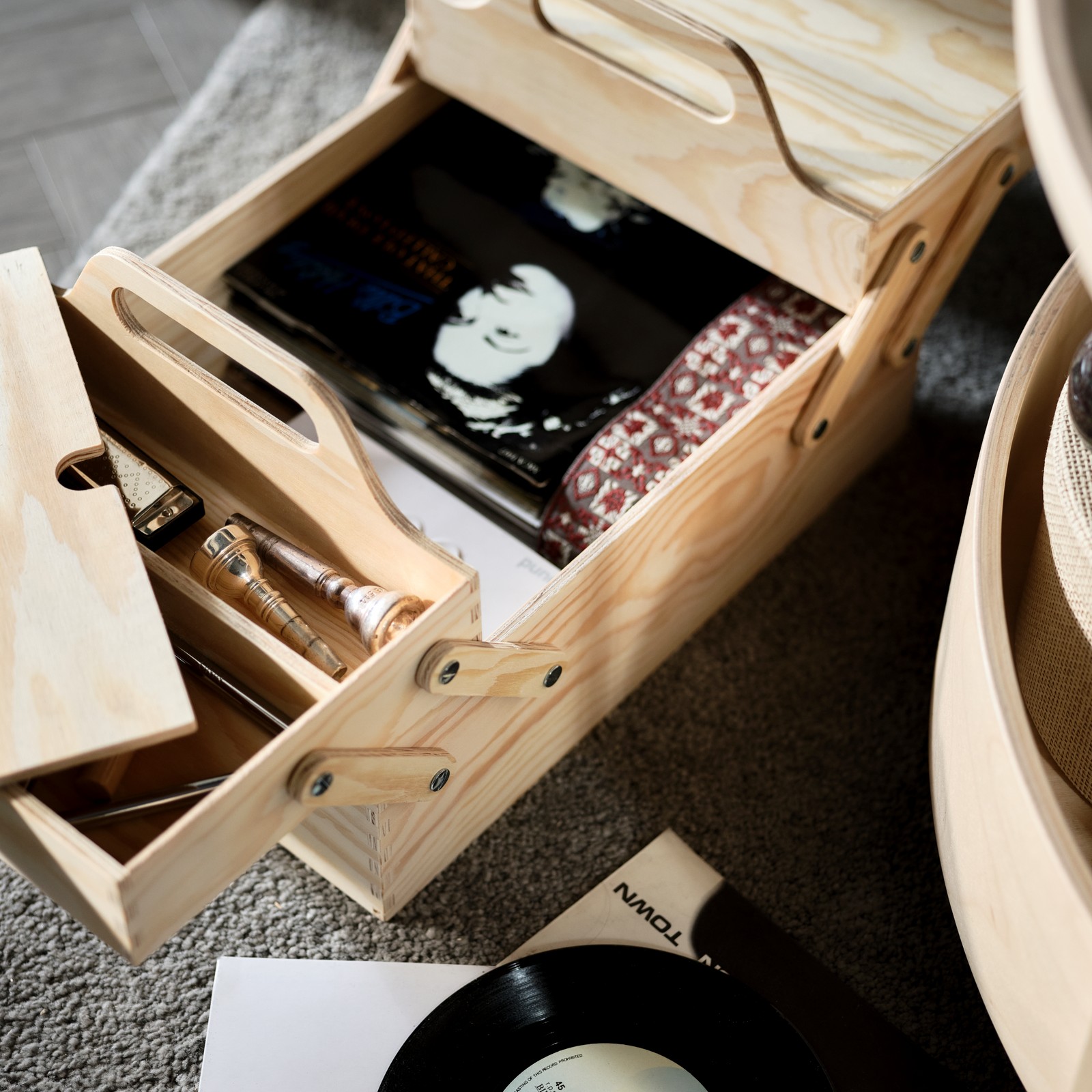 A natural-plywood KLÄMMEMACKA desk organiser stands on a rug with its sections parted, revealing musical accessories ins