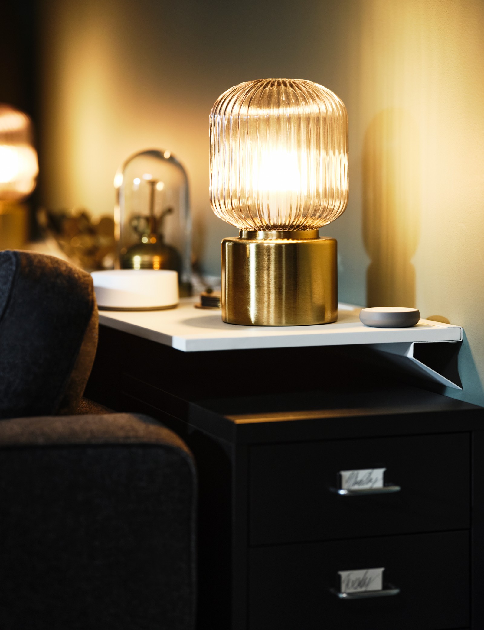 SOLKLINT brass table lamps and other decorative items sit on a wall shelf. Beneath the shelf stands a HELMER drawer unit