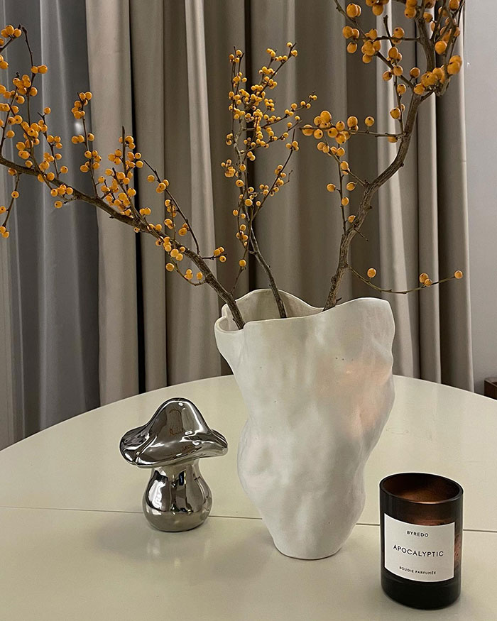 Handmade white vase with branches on table beside metallic mushroom and scented candle, showcasing home decor ideas and