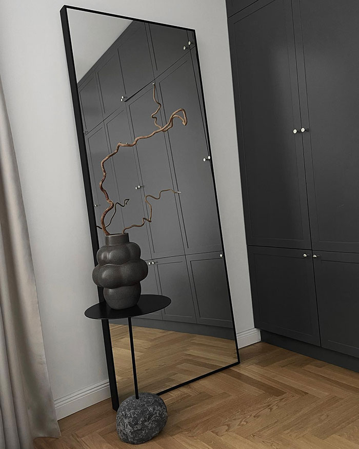 Large floor mirror leaning against bedroom wall with modern decor and minimalist design reflecting cabinetry and wooden