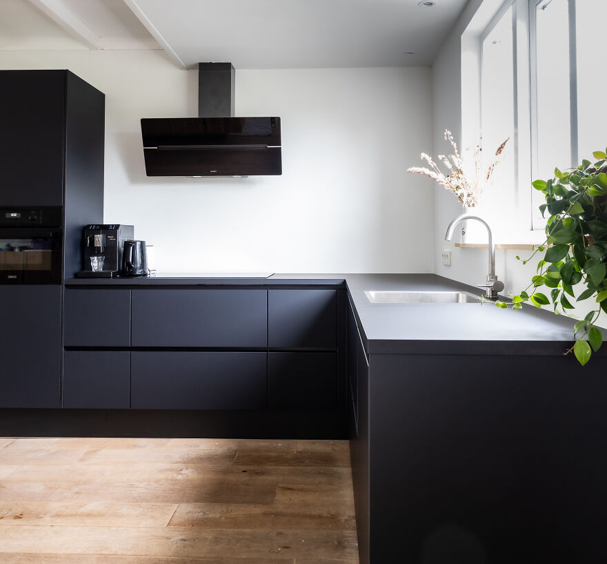 Black modern kitchen cabinets with sleek design in a bright space featuring white walls and natural light from a large w