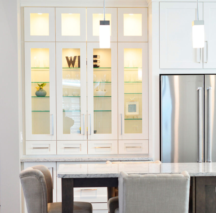 Modern glass kitchen cabinets with white frames and built-in lighting in a stylish, renovated kitchen space.